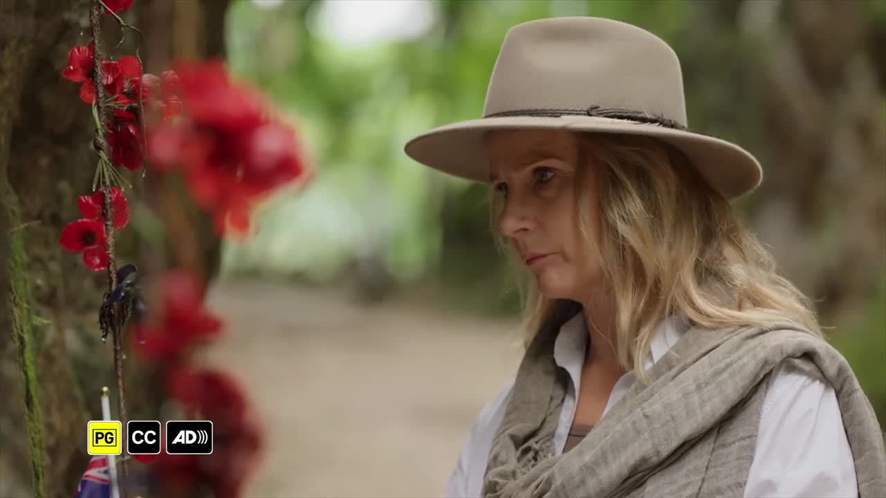 A woman in a hat, draped in a scarf, looks thoughtfully towards a display of red poppies. The scene feels like it's from an ABC Australia production, likely a documentary or drama.
