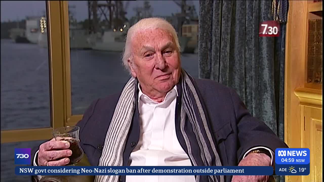 The man in the jacket and scarf is holding a glass, looking towards the camera on ABC News. Behind him, a window shows a dark harbor scene.
The man in the jacket and scarf is holding a glass, looking towards the camera on ABC News. Behind him, a window shows a dark harbor scene.