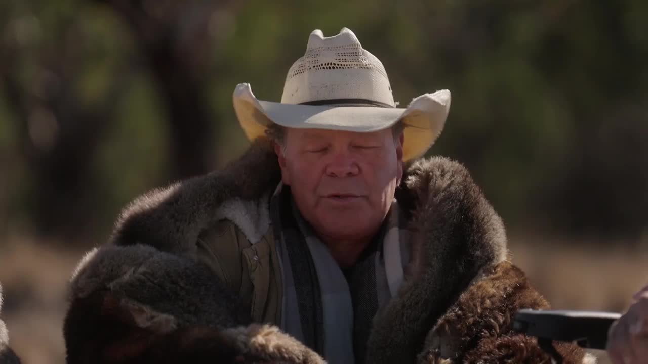 A man in a cowboy hat and fur coat sits with his eyes closed. A furry creature rests against his shoulder.
A man in a cowboy hat and fur coat sits with his eyes closed. A furry creature rests against his shoulder.