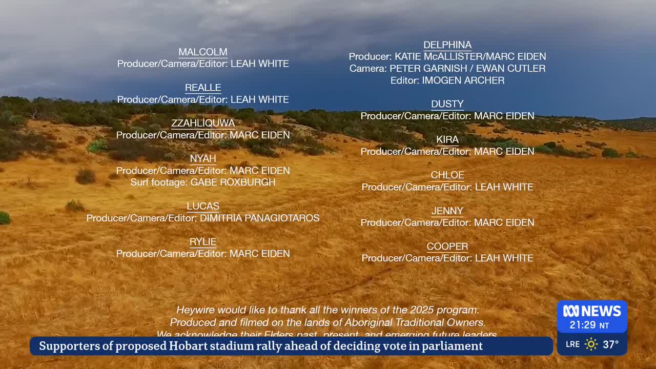 The credits for an ABC Australia program scroll over a landscape of dry, yellow grass and low hills under a cloudy sky. Below, a news ticker mentions a proposed stadium rally in Hobart.
The credits for an ABC Australia program scroll over a landscape of dry, yellow grass and low hills under a cloudy sky. Below, a news ticker mentions a proposed stadium rally in Hobart.