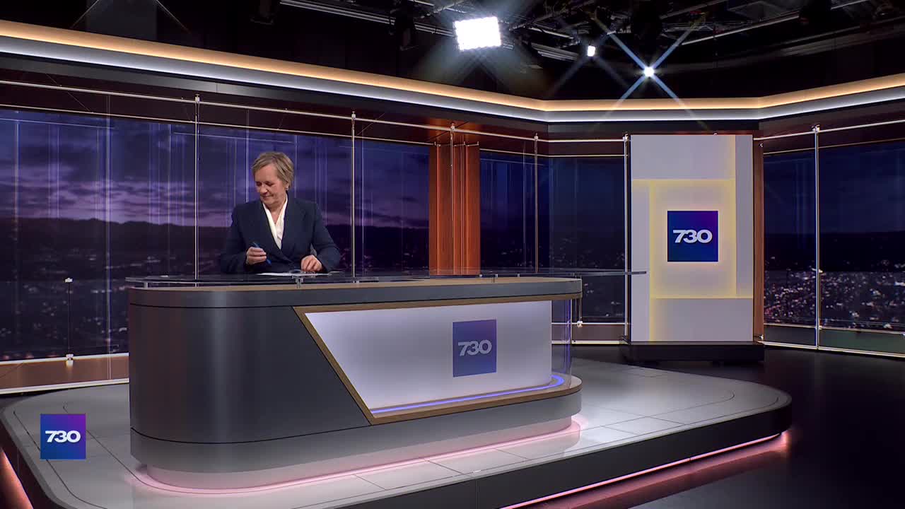 The presenter at the ABC Australia news desk is poised, pen in hand, looking down at her notes. The "7.30" logo is prominent on the desk and backdrop.
The presenter at the ABC Australia news desk is poised, pen in hand, looking down at her notes. The "7.30" logo is prominent on the desk and backdrop.