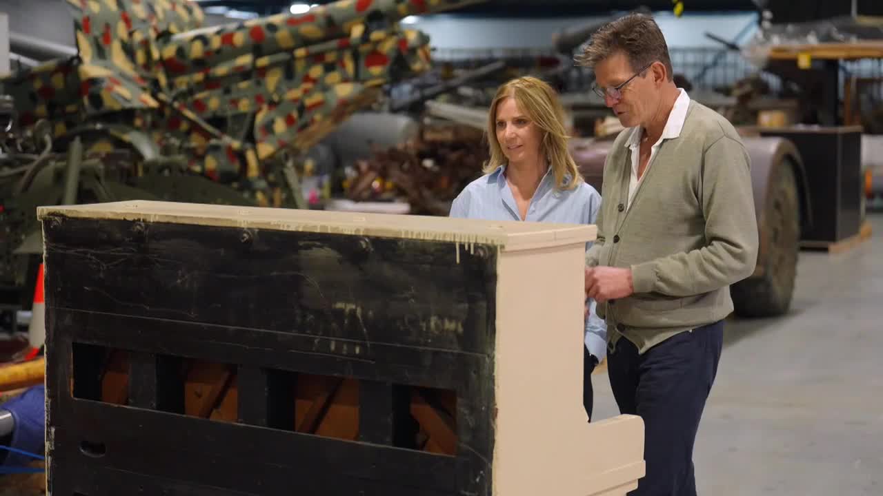 A man and a woman are standing beside a piano, examining it closely. The instrument's black front contrasts with its cream-colored sides.
A man and a woman are standing beside a piano, examining it closely. The instrument's black front contrasts with its cream-colored sides.