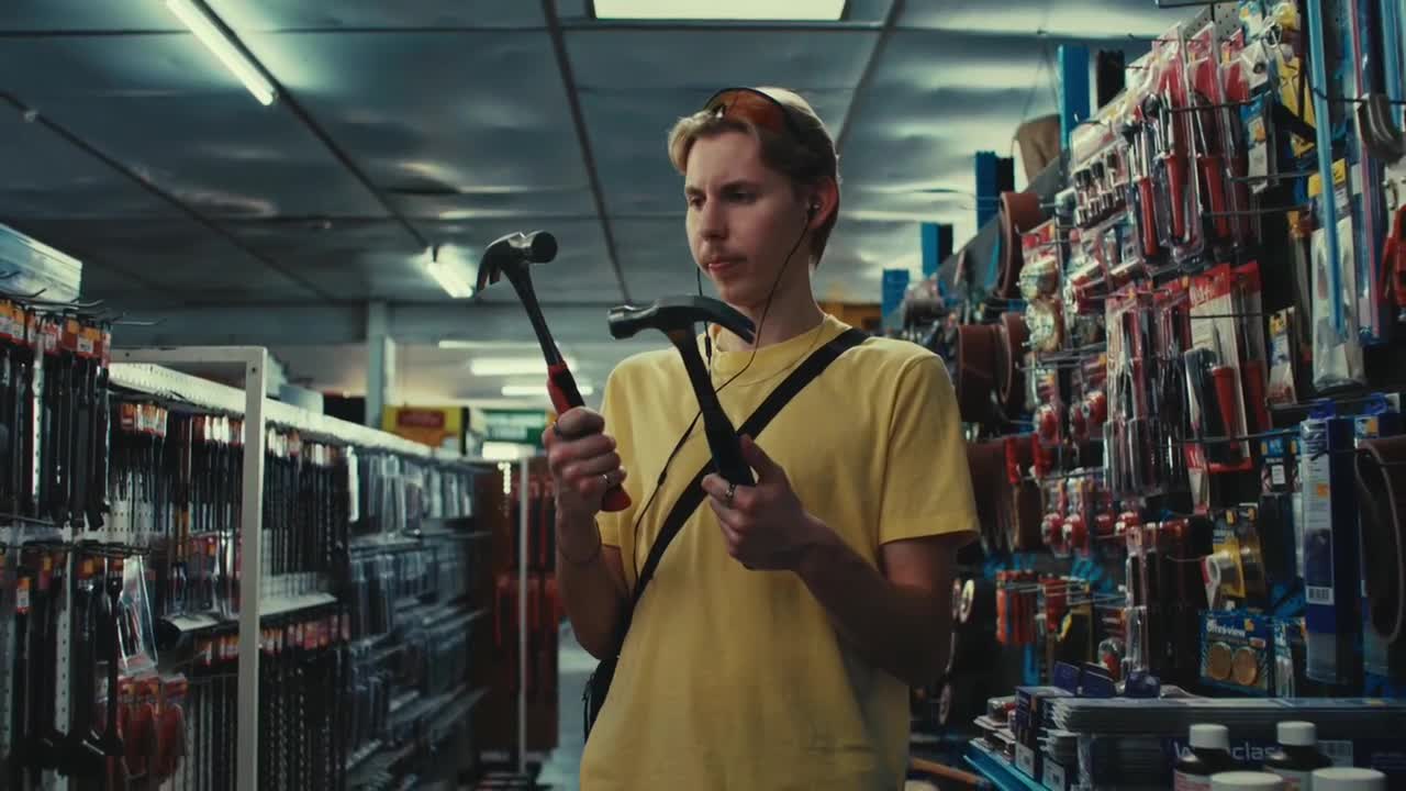 A young man in a yellow shirt holds up two hammers, comparing them in a hardware store aisle. He's got earbuds in and a shoulder bag slung across his chest.
A young man in a yellow shirt holds up two hammers, comparing them in a hardware store aisle. He's got earbuds in and a shoulder bag slung across his chest.