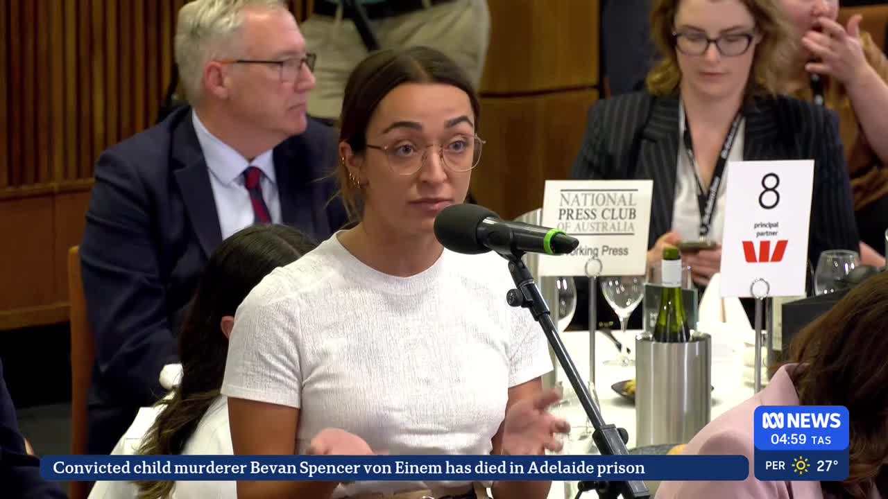 A woman with glasses speaks into a microphone, her hands gesturing as she addresses the room. The ABC News logo is visible in the corner, with a headline about a death in an Adelaide prison.
A woman with glasses speaks into a microphone, her hands gesturing as she addresses the room. The ABC News logo is visible in the corner, with a headline about a death in an Adelaide prison.