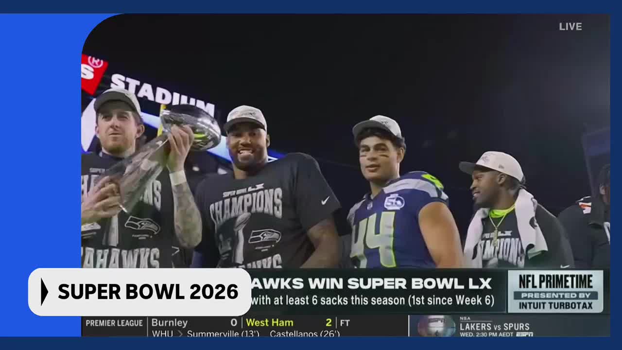 The Seahawks players are celebrating, one holding up the Super Bowl trophy. Their team's victory is being broadcast live, a moment of triumph for the fans.