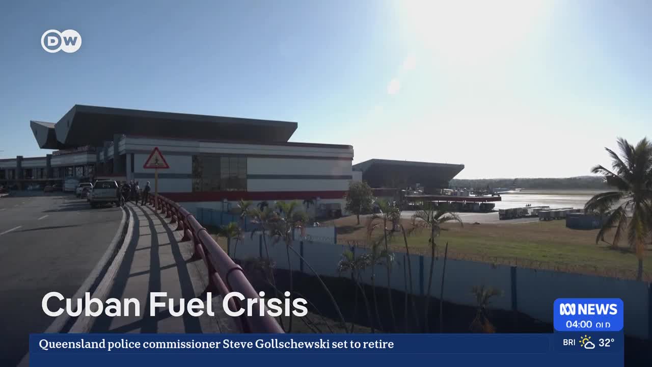 A few cars are parked near the entrance of a modern airport terminal under a bright sky.  Palm trees sway gently in the distance.