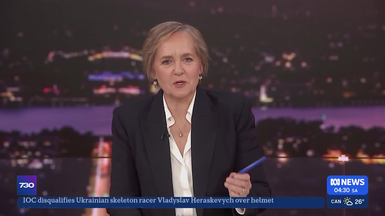 A woman in a dark blazer speaks directly to me, holding a blue pen. Behind her, a city skyline glows under a dark sky.