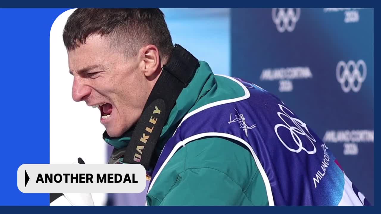 The Australian athlete roars, his face contorted with emotion as he clutches a medal. The Olympic rings are visible on his jacket, a testament to his achievement.