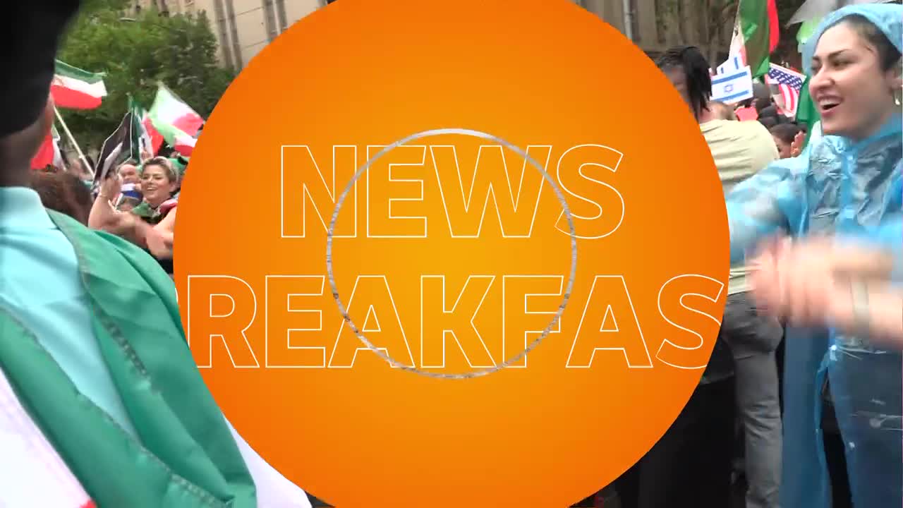 A crowd waves flags, some green, white, and red, while others are the Israeli flag. A woman in a bright blue poncho laughs and claps her hands. A crowd waves flags, some green, white, and red, while others are the Israeli flag. A woman in a bright blue poncho laughs and claps her hands.