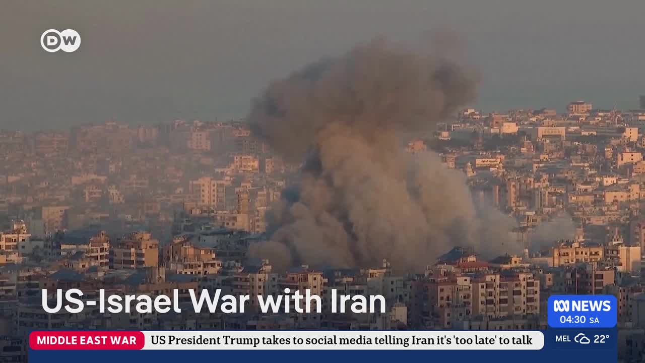 Thick plumes of grey smoke billow upwards from a city skyline. Buildings are densely packed, some showing signs of damage.