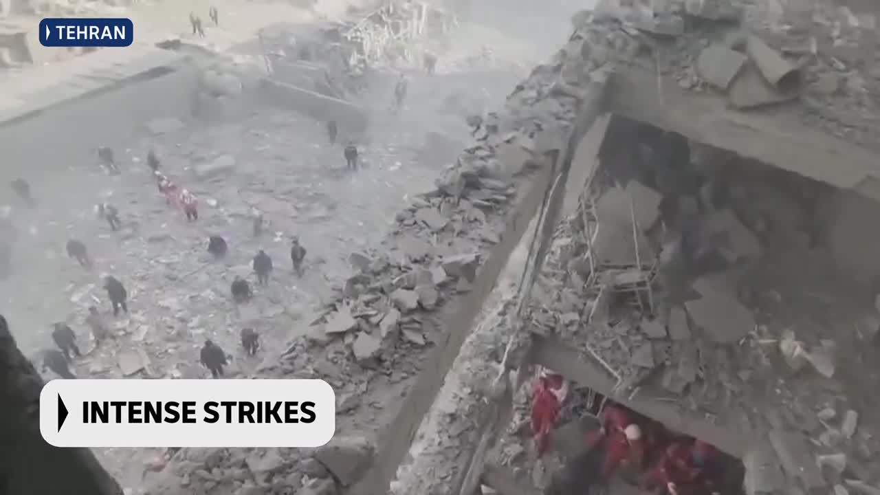 People in red vests are sifting through rubble in Tehran. Dust hangs heavy in the air, obscuring the full extent of the devastation.