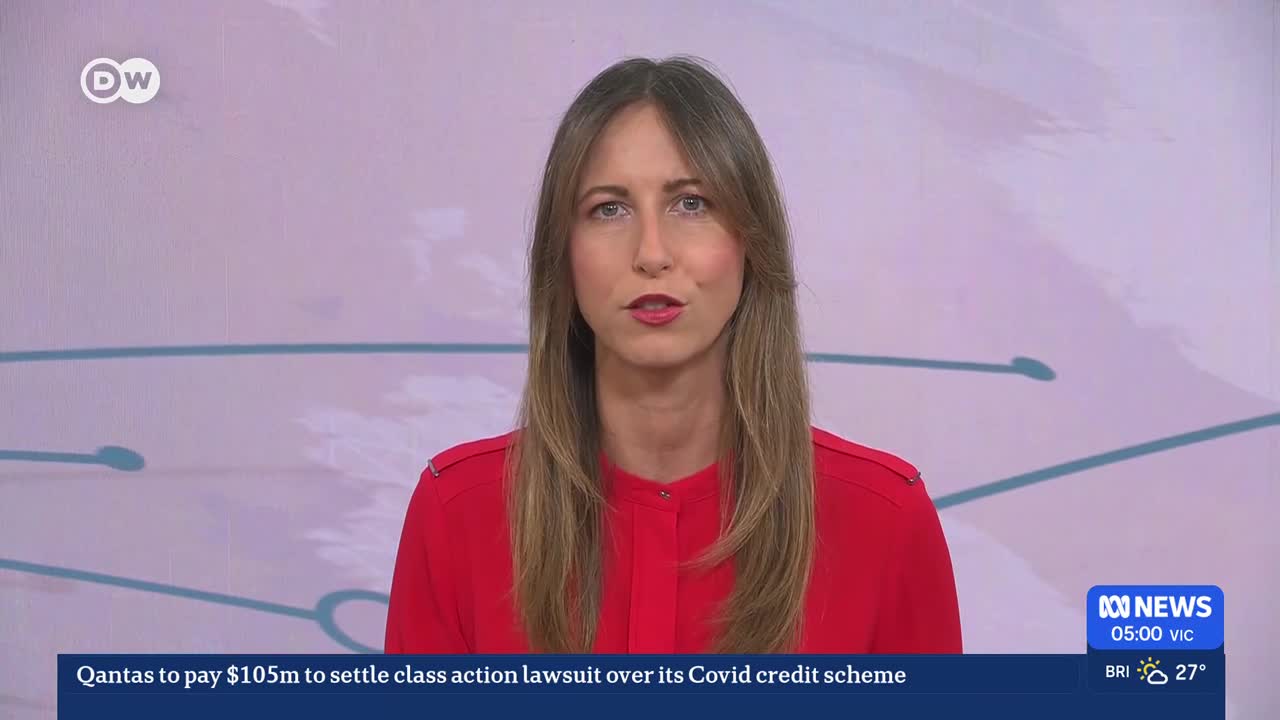 A woman in a bright red shirt speaks directly to the camera. Below her, a news ticker reports Qantas will pay $105 million to settle a class action lawsuit.