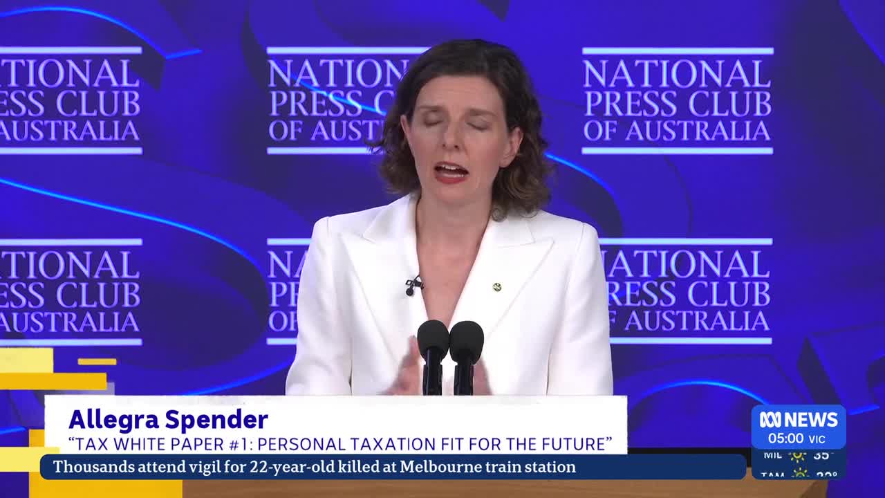 Allegra Spender stands at a podium, speaking into two microphones against a backdrop of the National Press Club of Australia logo. A news ticker at the bottom of the screen reports on her speech and a vigil in Melbourne. Allegra Spender stands at a podium, speaking into two microphones against a backdrop of the National Press Club of Australia logo. A news ticker at the bottom of the screen reports on her speech and a vigil in Melbourne.