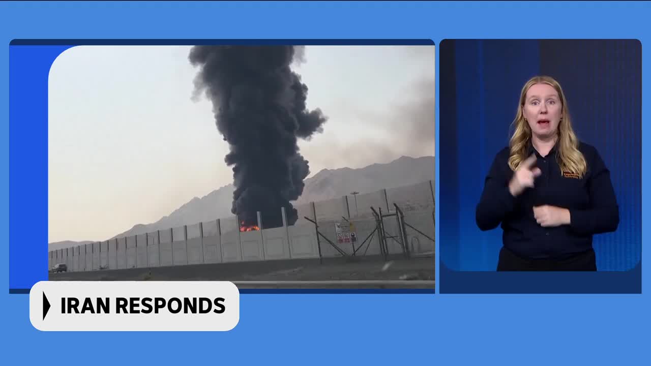 Thick, black smoke billows upwards from behind a concrete wall. Flames are visible at the base of the smoke plume. Thick, black smoke billows upwards from behind a concrete wall. Flames are visible at the base of the smoke plume.