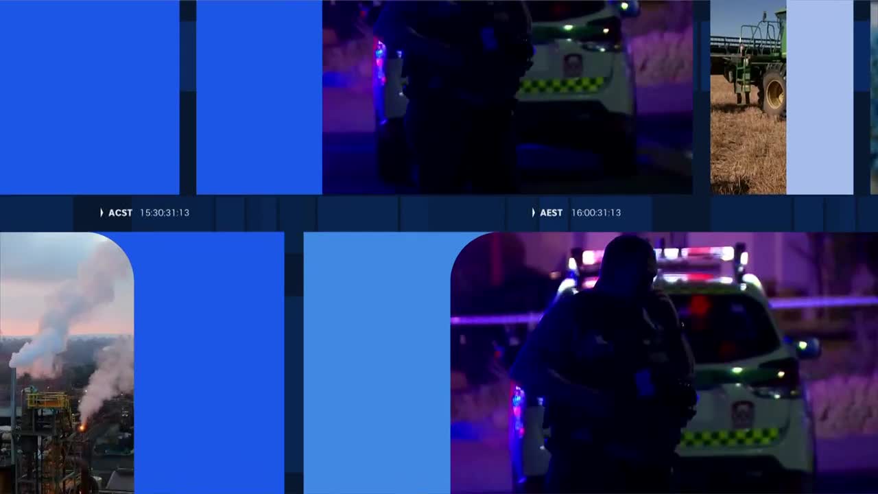 Police lights flash around a patrol car as an officer stands in silhouette. Smoke billows from a large industrial plant in the distance.