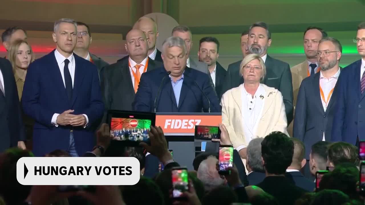 The man at the podium, Viktor Orbán, speaks to a crowd as supporters hold up phones to record. A banner behind him reads "FIDESZ," the name of his political party.