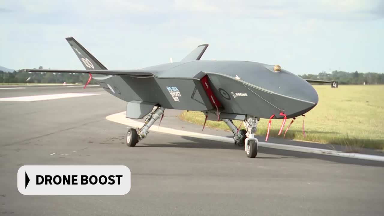 A large, dark grey drone sits on an Australian tarmac, its landing gear extended. Red tags hang from its wings, and the "Boeing" logo is visible on its side.