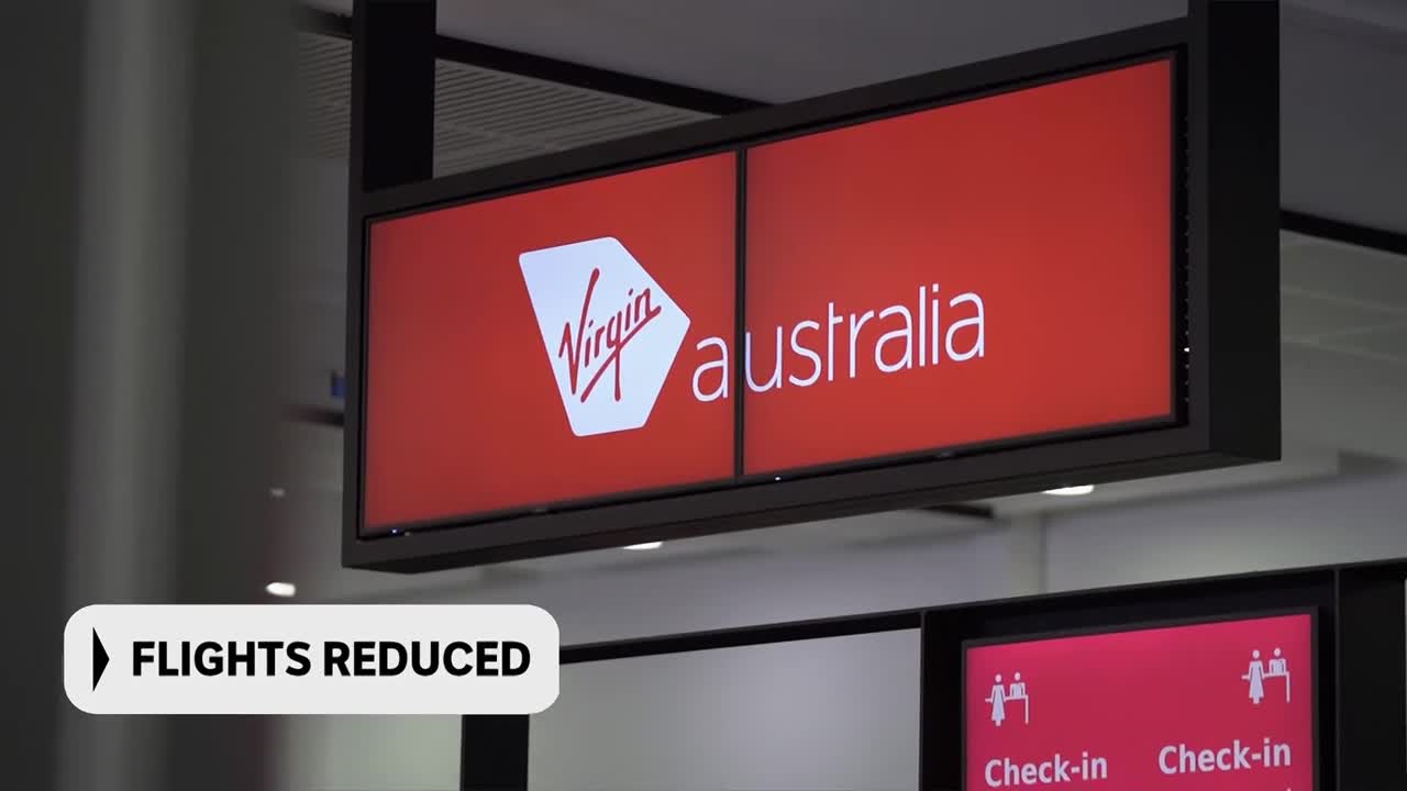 A bright red sign overhead displays the Virgin Australia logo and name. Below it, a smaller screen shows "FLIGHTS REDUCED" in white text.
