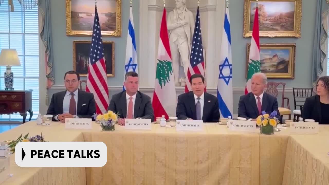 Five people sit at a long table, American and Israeli flags behind them. The man in the center speaks, his hands resting on the table.