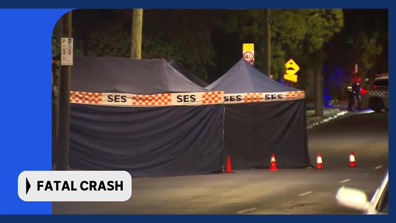 Emergency tents are set up on the side of the road, marked with "SES" tape. A police car with flashing blue lights sits nearby, and a person in uniform stands beside it.