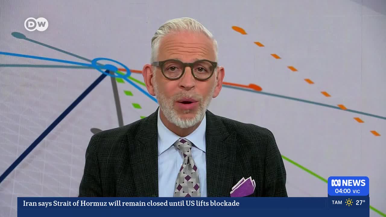 A man with grey hair and glasses speaks directly to the camera. A news ticker at the bottom of the screen reads "Iran says Strait of Hormuz will remain closed until US lifts blockade."