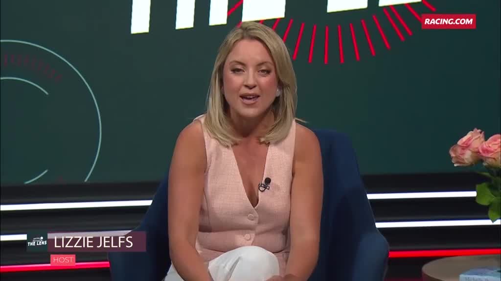 Lizzie Jelfs, the host, is seated and speaking on Racing.com. Her light pink top and white pants contrast with the dark blue chair and background.
