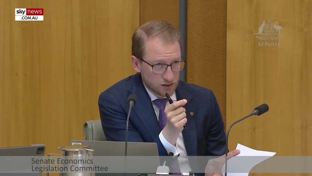 On Sky News Extra 1, a man in a blue suit gestures with a pen, speaking into a microphone. He holds a piece of paper, part of a Senate Economics Legislation Committee meeting in Australia.
