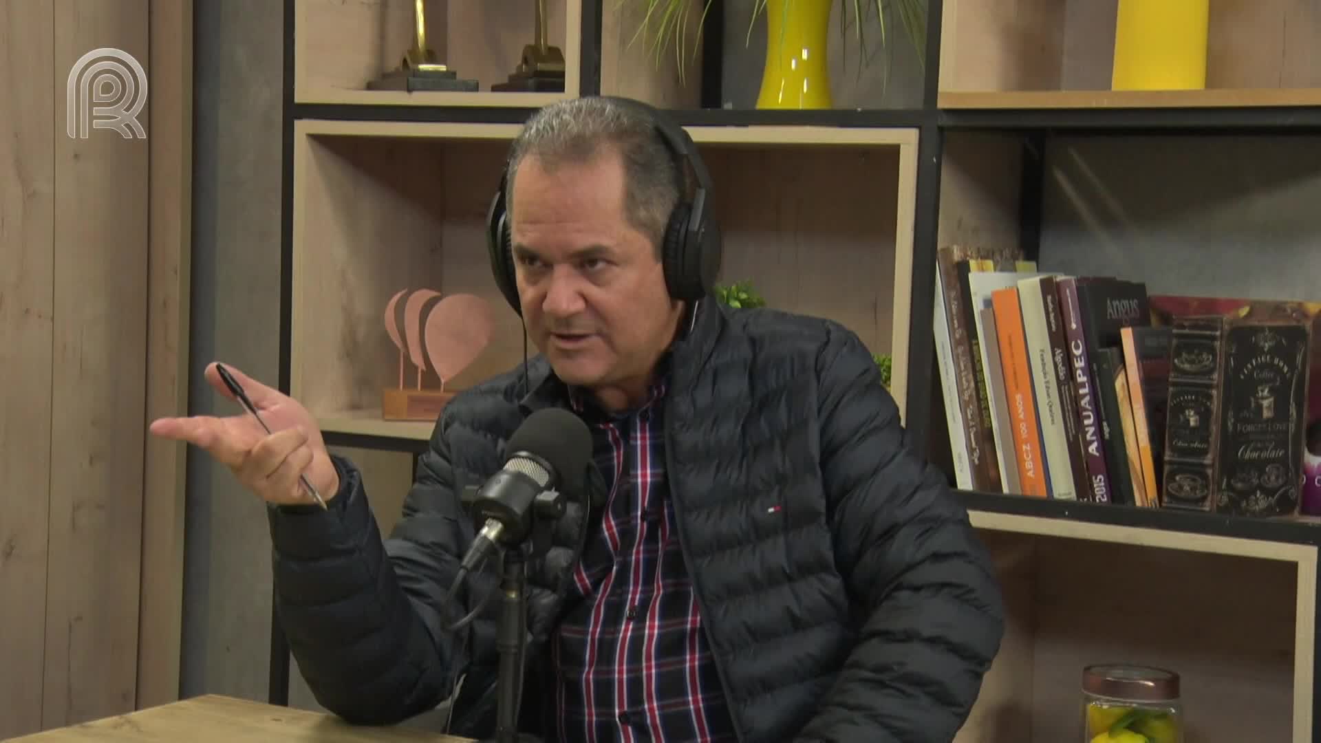 The man in the puffy jacket gestures with a pen, talking into a microphone. He's wearing headphones and seems to be on a broadcast from Brazil.

