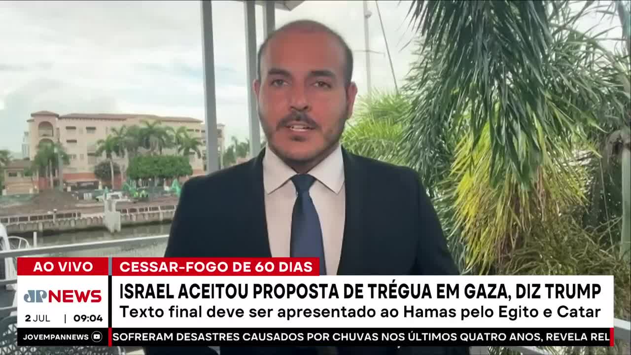 A man in a dark suit and tie speaks directly to the camera, framed by a window and greenery. The Jovem Pan News logo and a headline about a Gaza ceasefire flash at the bottom of the screen.
