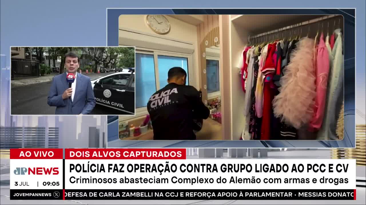 A Polícia Civil officer is inside a room, his back to the camera, examining something near a window. Across the room, a rack of colorful clothing hangs in a closet, as Jovem Pan News reports on the raid in Brazil.
