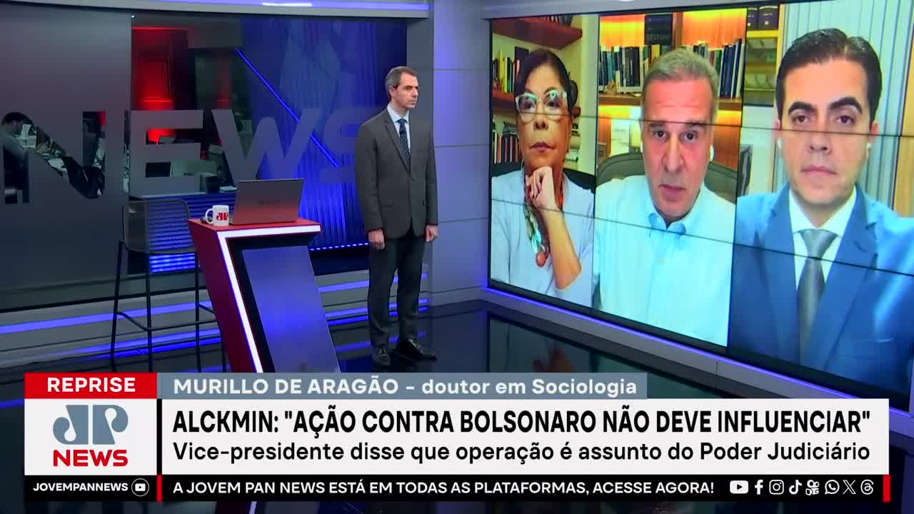 A man in a suit stands facing the camera, while a screen behind him displays three people in a video call. The Jovem Pan News logo is visible, along with text about a vice-president and a legal action.
