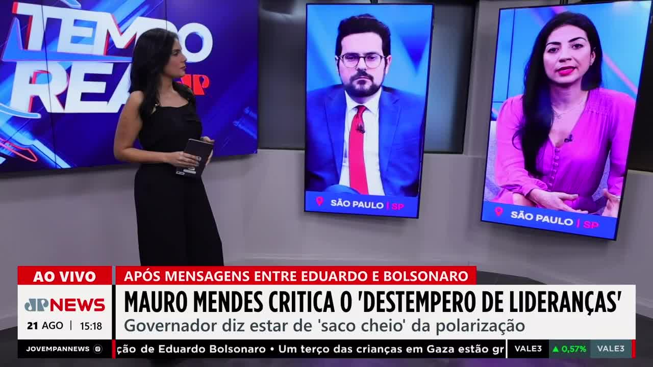 A woman in a black jumpsuit stands in a studio, holding a tablet, while two other speakers appear on screens behind her. Jovem Pan News is reporting live from Brazil, with the headline "Mauro Mendes Critica o 'Destempero de Lideranças.'"
