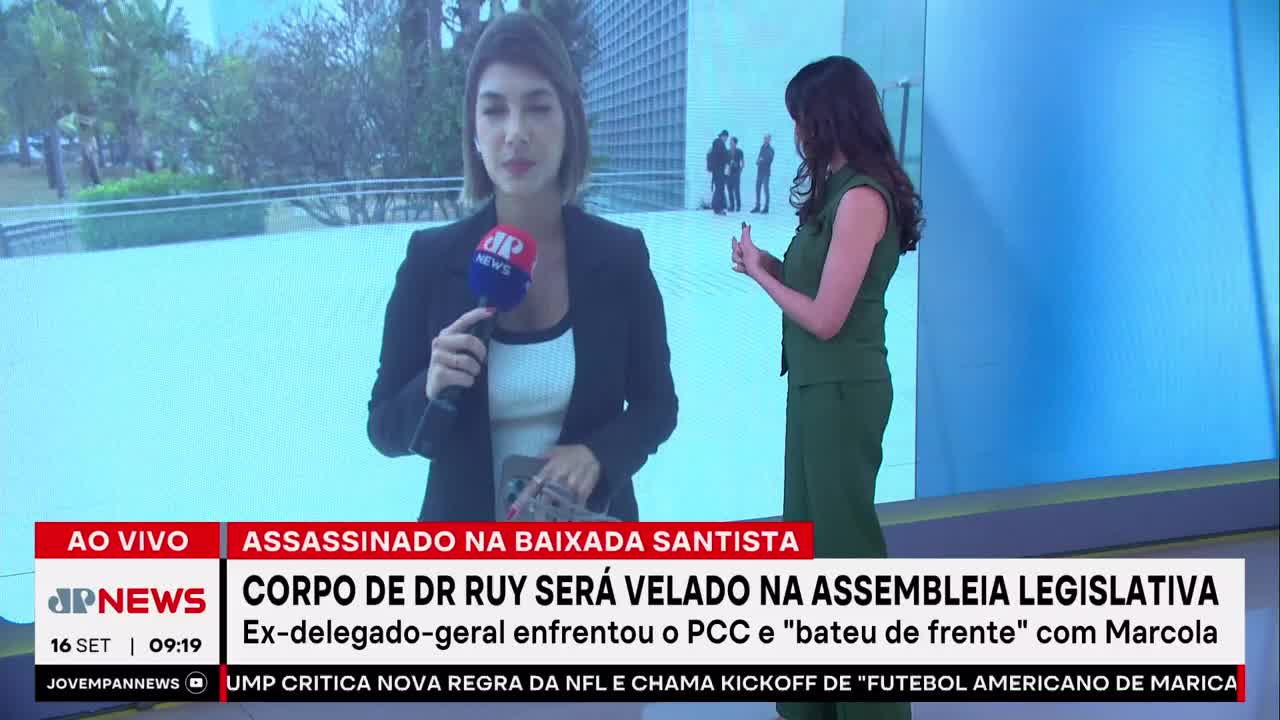The news anchor in a black blazer holds a microphone, speaking directly to the camera. Behind her, another woman in green gestures towards a building, while the Jovem Pan News banner reports on a murder in Baixada Santista.
