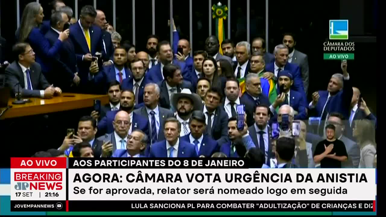 A crowd of suited men and women in the Brazilian Câmara dos Deputados is packed together, many holding up phones. Jovem Pan News reports live as they vote on an amnesty.
