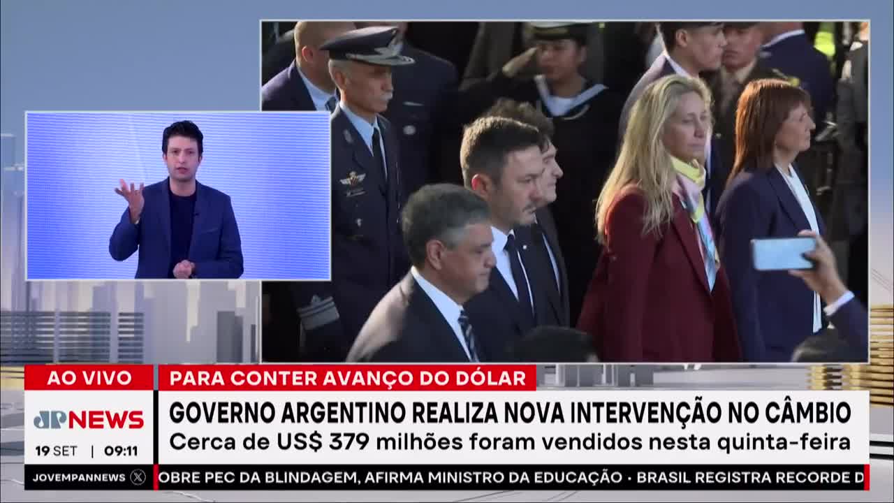 A news anchor gestures emphatically, his image superimposed over a group of people walking.  A woman in a red blazer and a woman in a blue blazer are among those being filmed.
