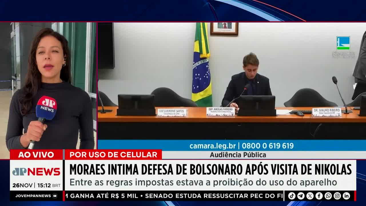 A Jovem Pan News reporter stands with a microphone, reporting live from Brazil. In the background, a man in a suit sits at a table in what appears to be a public hearing, with a Brazilian flag behind him.
A Jovem Pan News reporter stands with a microphone, reporting live from Brazil. In the background, a man in a suit sits at a table in what appears to be a public hearing, with a Brazilian flag behind him.