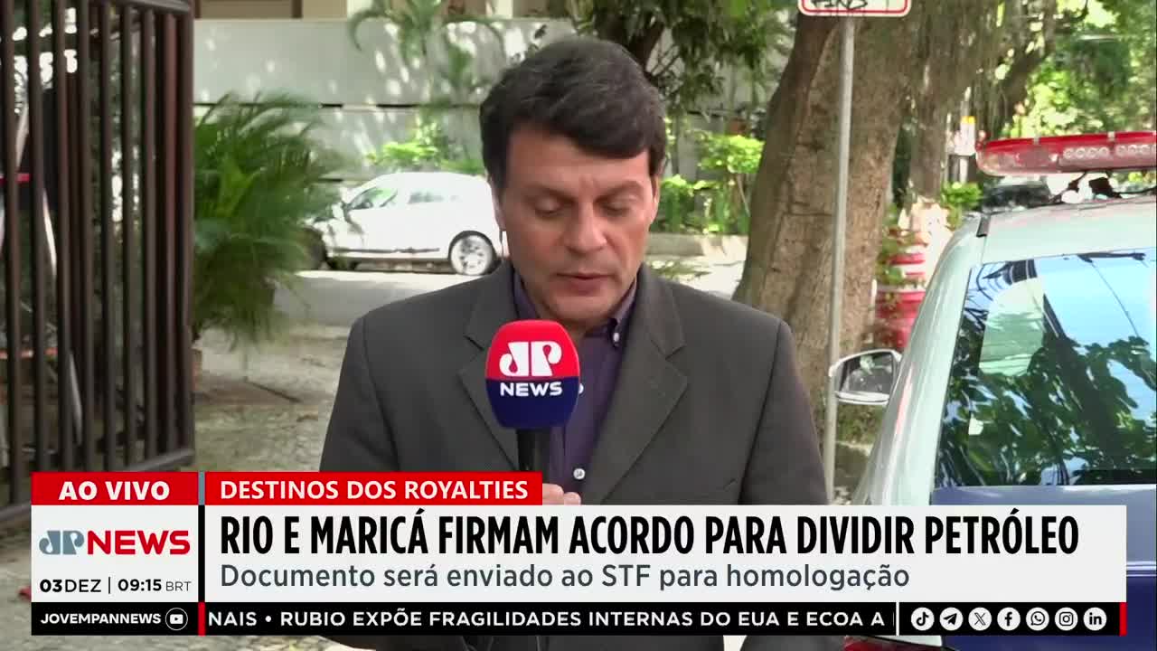 A news anchor, holding a microphone with the "JP News" logo, is speaking live on location. Behind him, a car and a gated entrance are visible, with a banner discussing the division of oil royalties in Rio and Maricá.
A news anchor, holding a microphone with the "JP News" logo, is speaking live on location. Behind him, a car and a gated entrance are visible, with a banner discussing the division of oil royalties in Rio and Maricá.