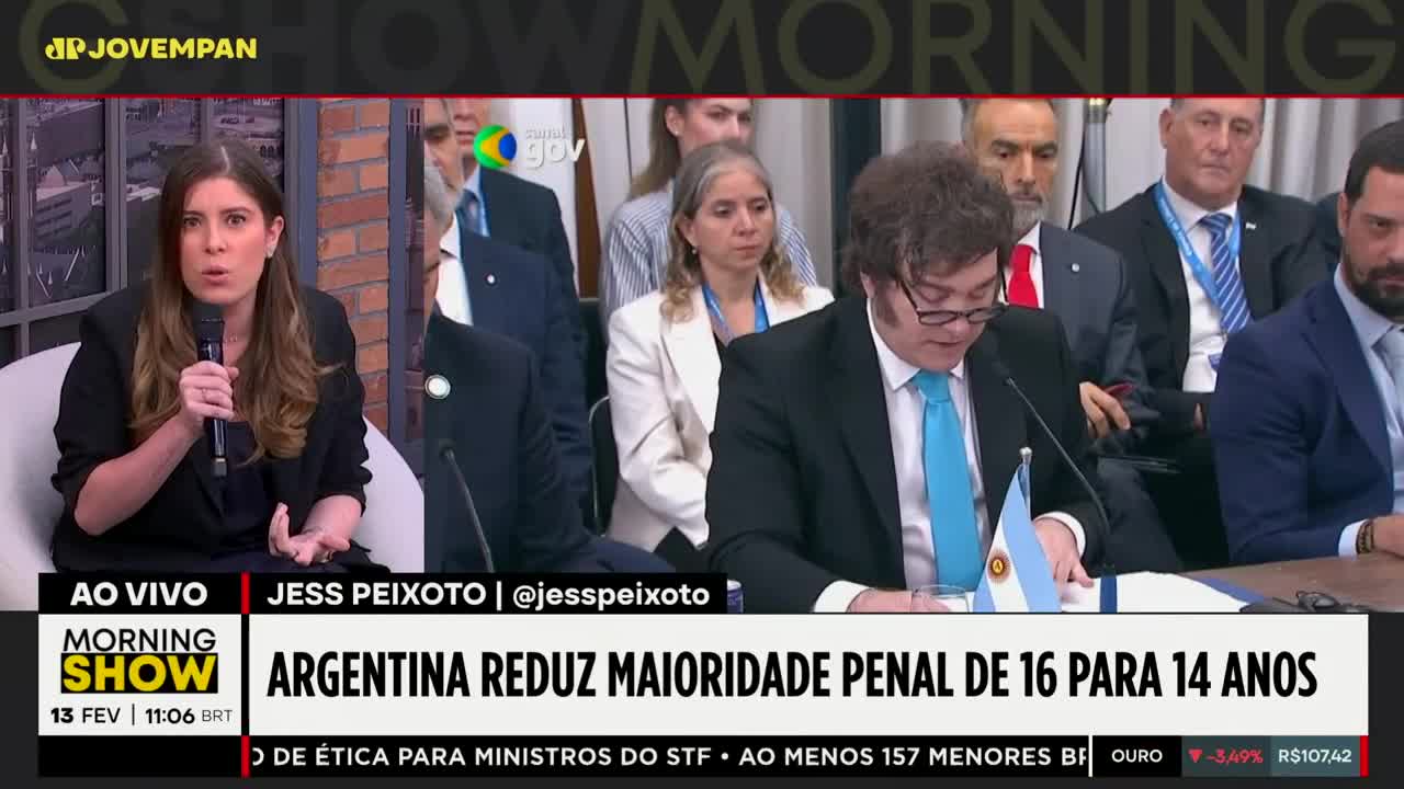 A woman in a black jacket speaks into a microphone, gesturing with her hands. Beside her, a man in a suit and tie looks down at papers, with an Argentinian flag on the table. A woman in a black jacket speaks into a microphone, gesturing with her hands. Beside her, a man in a suit and tie looks down at papers, with an Argentinian flag on the table.