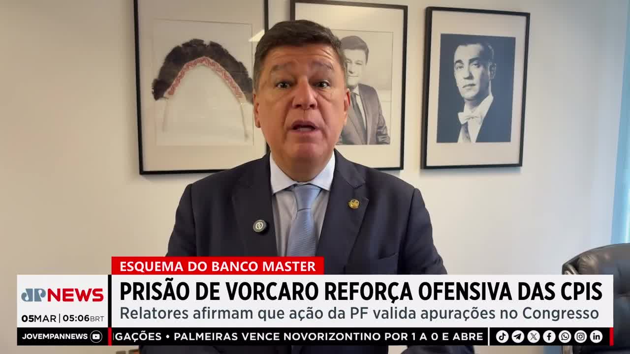 A man in a suit speaks directly to the camera, his words overlaid with a Jovem Pan News chyron. Behind him, framed portraits hang on a light-colored wall.