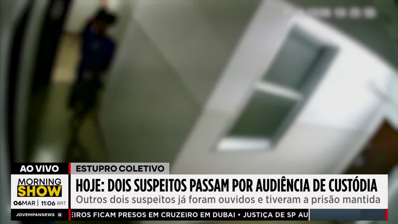 A person in a blue shirt and dark shorts walks down a hallway. The Jovem Pan News broadcast reports on two suspects undergoing a custody hearing.