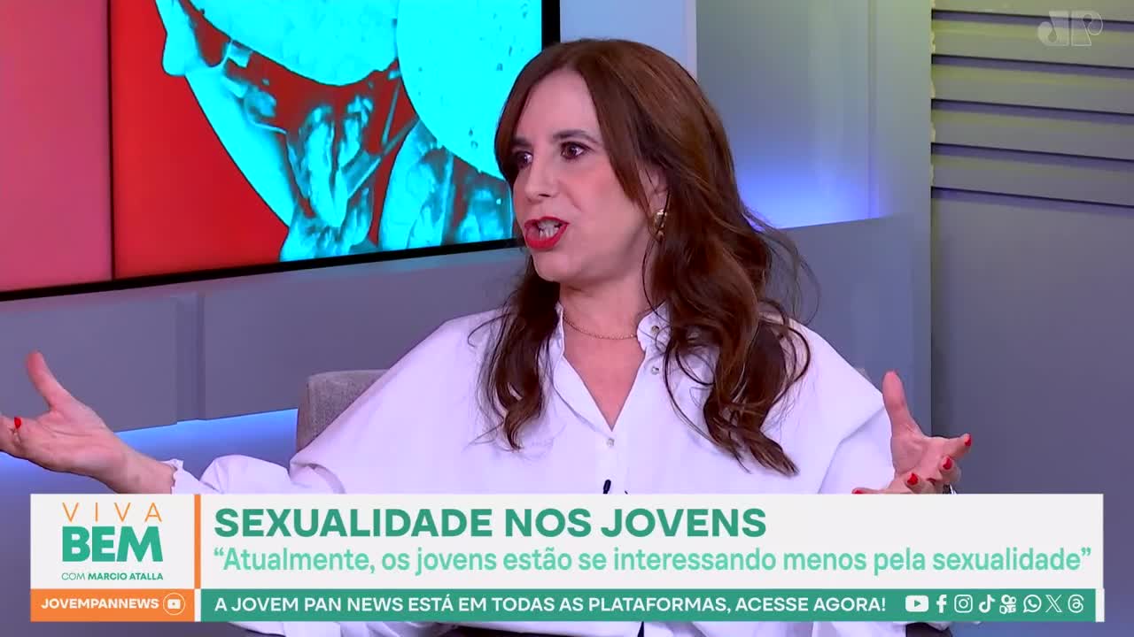 A woman with auburn hair gestures with both hands as she speaks, her white shirt open at the collar. A graphic overlay from Jovem Pan News displays the title "SEXUALIDADE NOS JOVENS."