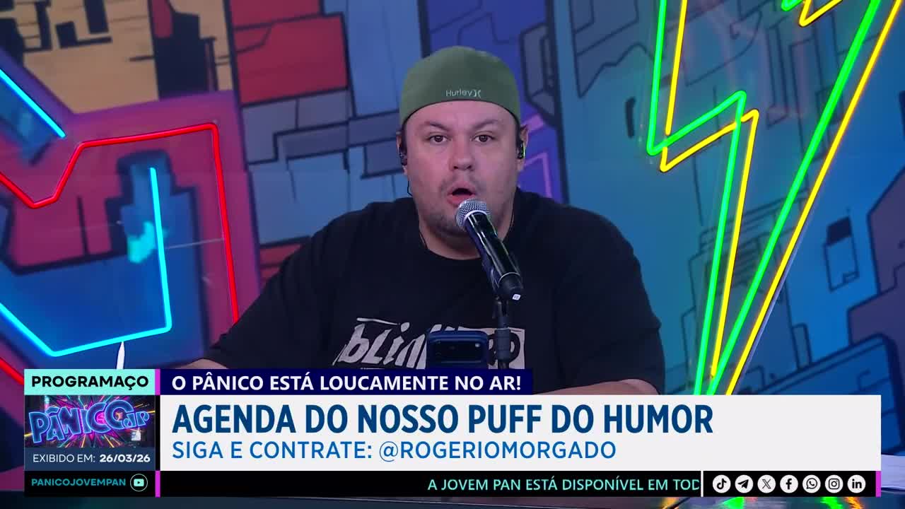 A man in a green cap speaks into a microphone on a brightly lit set. Text on the screen announces "O Pânico está loucamente no ar!" and "Agenda do nosso puff do humor." A man in a green cap speaks into a microphone on a brightly lit set. Text on the screen announces "O Pânico está loucamente no ar!" and "Agenda do nosso puff do humor."