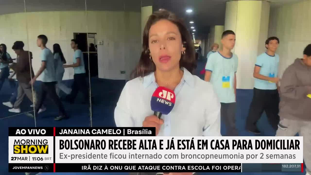 A group of young people in light blue shirts walk down a hallway, some with yellow and blue emblems on their shirts. A reporter stands in the foreground, holding a microphone with the JP News logo. A group of young people in light blue shirts walk down a hallway, some with yellow and blue emblems on their shirts. A reporter stands in the foreground, holding a microphone with the JP News logo.