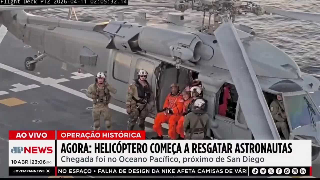 Soldiers in tactical gear stand by as astronauts in orange suits are helped out of a helicopter. The aircraft is parked on the deck of a ship, its rotors still.
