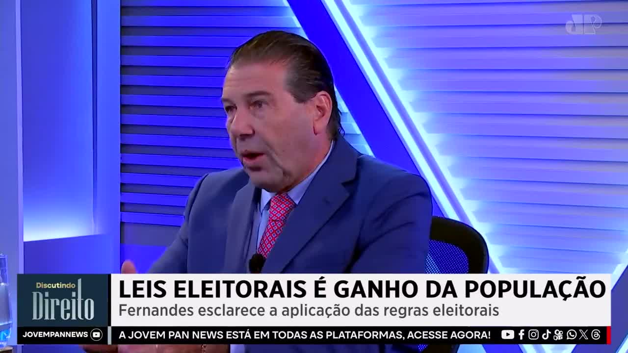 A man in a blue suit and pink tie speaks animatedly, his hand gesturing. The Jovem Pan News logo appears in the lower left corner, beneath a title about electoral laws.