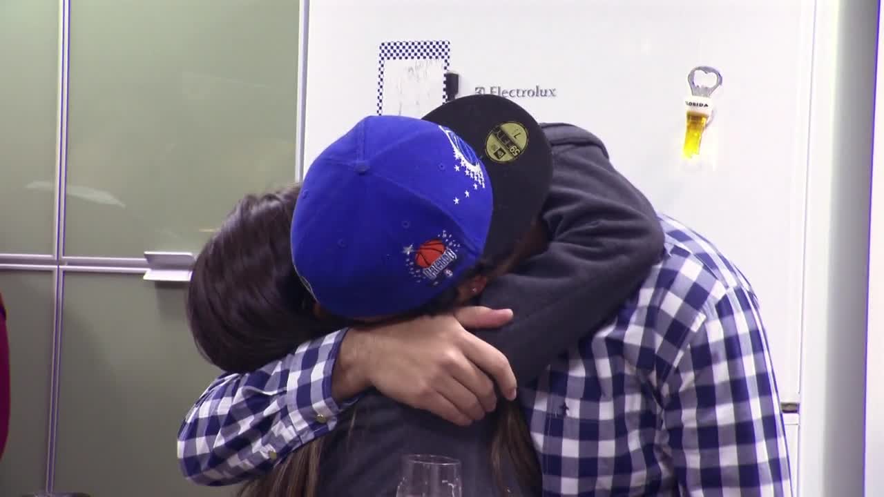 Two people are embracing tightly, their heads pressed together. One wears a blue basketball cap, the other a black one, as they're wrapped in a hug.
