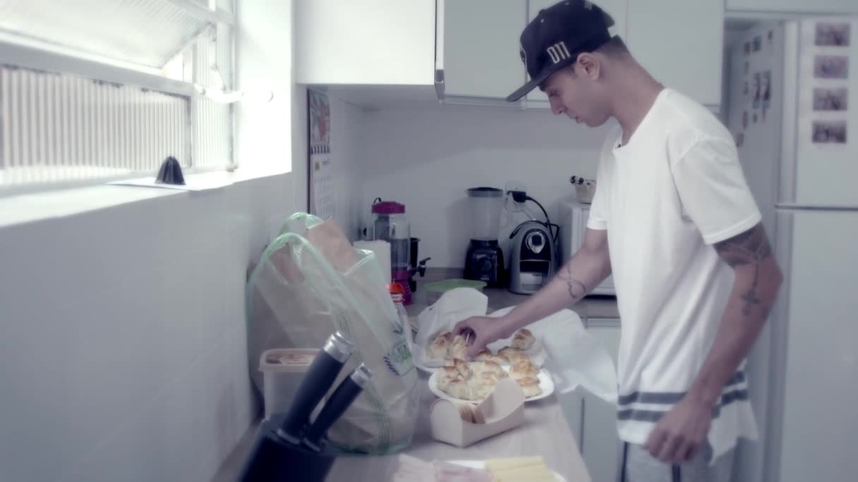 He's in a kitchen, reaching for a plate of what looks like pão de queijo, the Brazilian cheese bread. A few groceries are still in their bags on the counter, and the MTV Brazil star seems to be preparing a snack.
