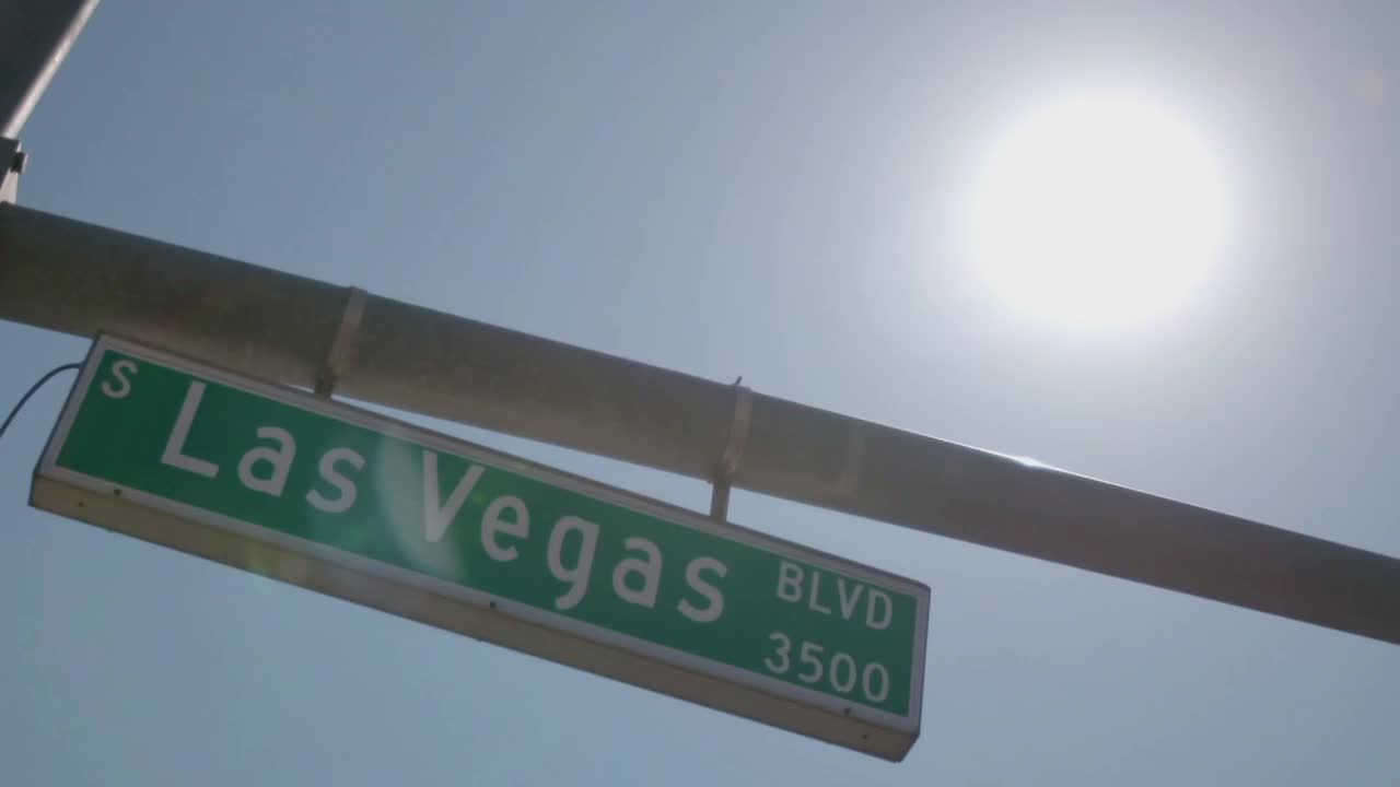 The sun is a blinding white orb, high in the sky. Below, a green street sign reads "Las Vegas Blvd."
