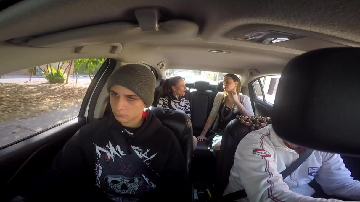 Inside a car, three young people are talking in the back seat, while a fourth person in a racing jacket is partially visible in the front. The guy in the beanie looks like he's not enjoying the ride.
