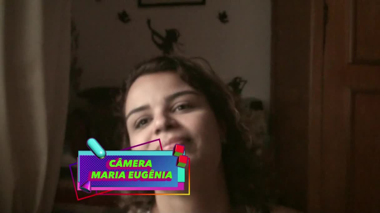 A woman with dark, curly hair smiles directly at the camera. A colorful graphic overlay identifies the camera as "CÂMERA MARIA EUGÊNIA."